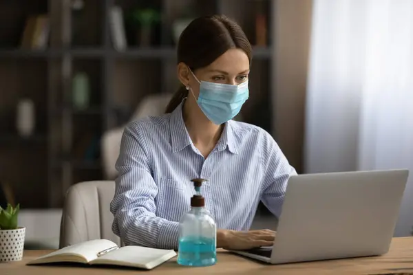 Female employee in facial mask work on laptop online — Stock Photo, Image