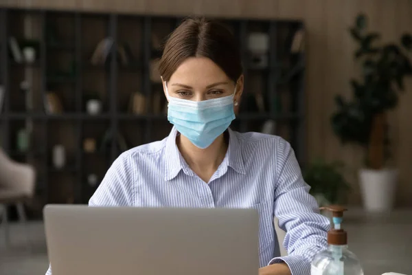 Caucasian female employee in facemask work on laptop — Stock Photo, Image