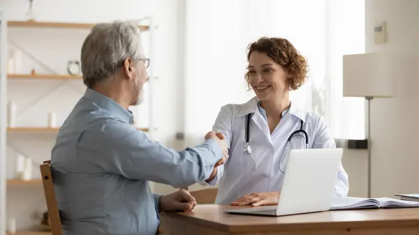 Mulher sorridente médico aperto de mão paciente masculino sênior — Fotografia de Stock