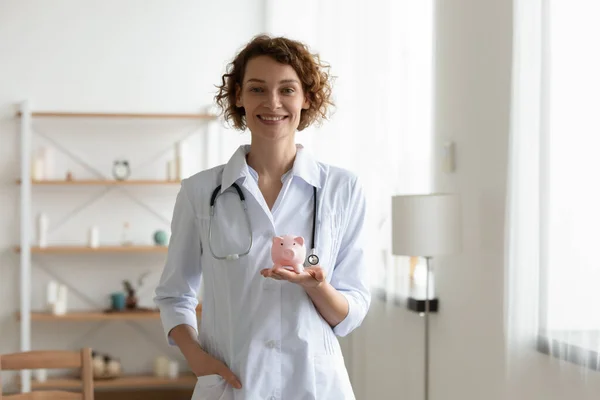 Retrato de sorridente fêmea médico segurar piggybank — Fotografia de Stock