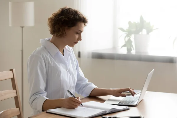 Médico femenino trabaja en nota de computadora en diario — Foto de Stock