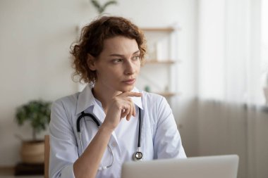 Düşünceli kadın doktor dizüstü bilgisayar üzerinde çalışıyor.