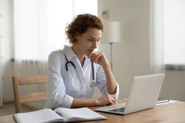 Düşünceli kadın pratisyen hekim dizüstü bilgisayar üzerinde çalışıyor.