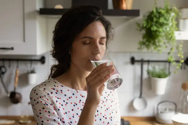 Dorstige duizendjarige vrouw drinken mineraalwater in de keuken uit glas — Stockfoto