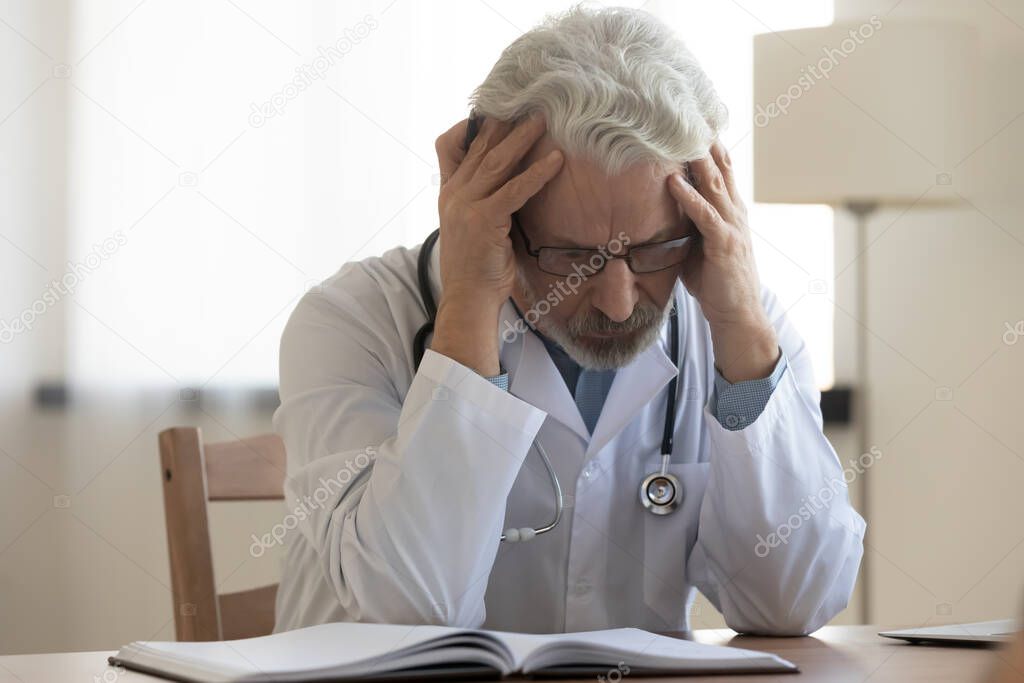 Unhappy senior doctor suffer from headache in clinic