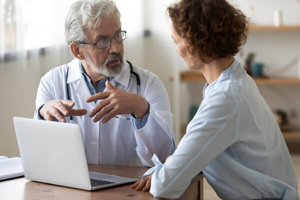 Senior doctor and patient discuss illness using laptop