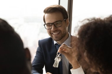 Gülümseyen beyaz bir emlakçı müşterilere anahtar veriyor.
