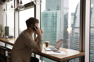 Arkadan bakan kendine güvenen işadamı telefonla konuşuyor, pencereden dışarı bakıyor