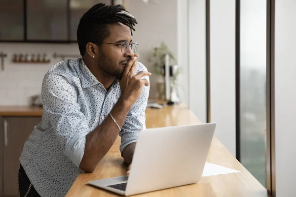 Close up dreamy African American man wearing glasses using laptop — Stock Photo, Image