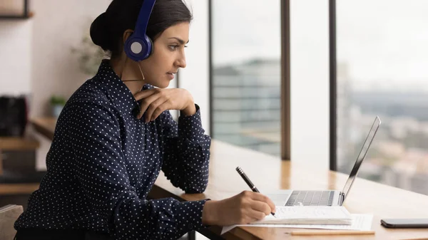 Close up focused Indian woman wearing headphones taking notes — Stock Photo, Image