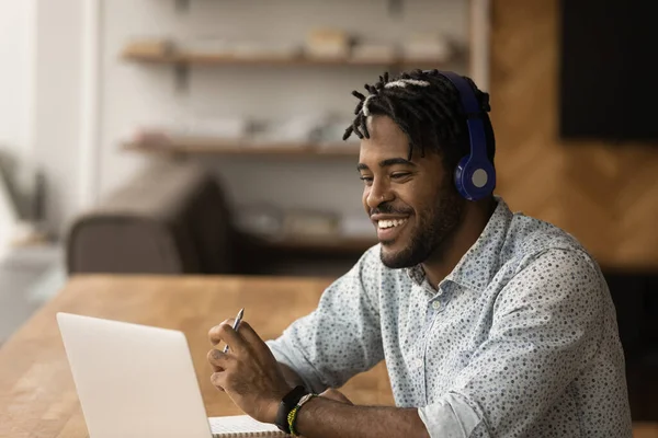 用笔记本电脑近距离观察戴着耳机、面带微笑的非裔美国人 — 图库照片