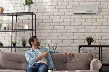 Mutlu genç adam kanepeye otur ve klimayı tut.