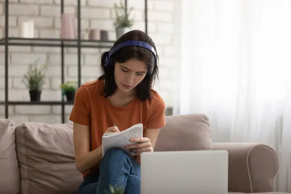 Jeune femme dans les écouteurs regarder la formation sur ordinateur portable prendre des notes — Photo