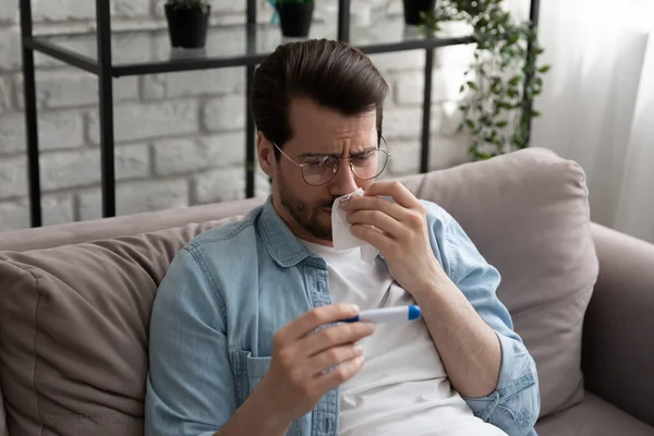 Тысячелетний человек чувствует себя плохо вытирать нос увидеть лихорадку на термометре — стоковое фото