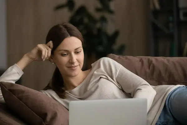 Donna felice rilassarsi sul divano utilizzando gadget per computer — Foto Stock