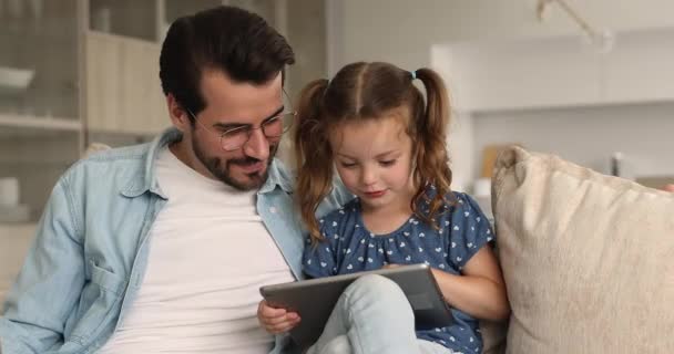 Тато проводить час з маленькою донькою, розслабляючись разом з планшетом — стокове відео