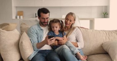 Çift ve kızı kanepede oturup akıllı telefon kullanarak eğleniyorlar.