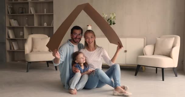 Familia feliz con hija sentada bajo el símbolo del techo de cartón — Vídeos de Stock