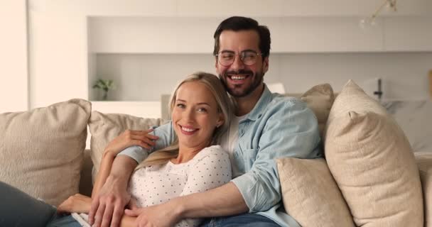Pasangan muda yang cantik jatuh cinta merangkul beristirahat di sofa — Stok Video
