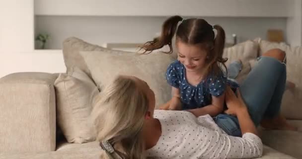 Anne kanepede uzanıyor ve küçük kızıyla oynuyor. — Stok video