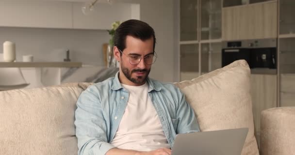 Seriöser Mann sitzt mit Laptop auf Couch und arbeitet von zu Hause — Stockvideo