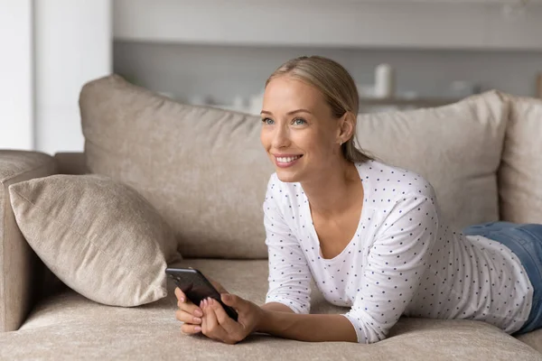Smiling woman relax on sofa using smartphone gadget