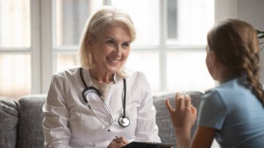 Gülümseyen kadın pratisyen hekim küçük kız hastaya danıştı