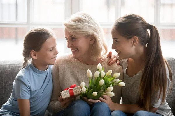Çocuk ve genç anne büyükannelerini hediyelerle selamlıyorlar. — Stok fotoğraf