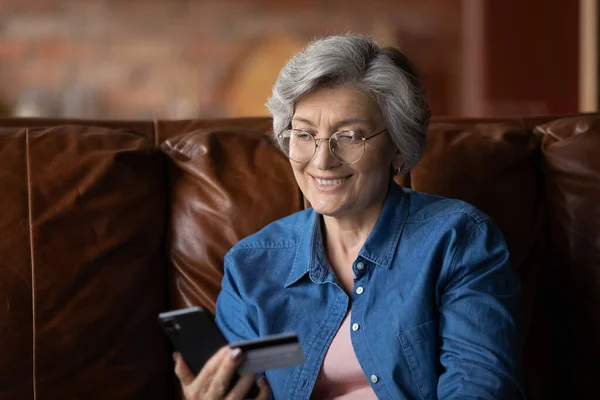 Уверенная пожилая латиноамериканка держит смартфон карты делать покупки в Интернете — стоковое фото