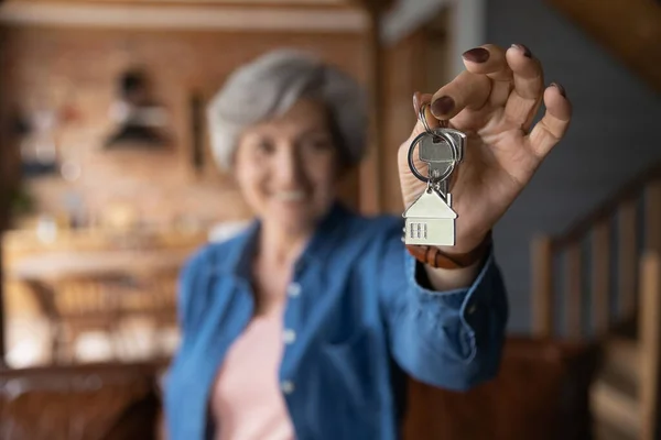 Glad äldre kvinnlig husägare poserar på landet stuga hålla nycklar — Stockfoto