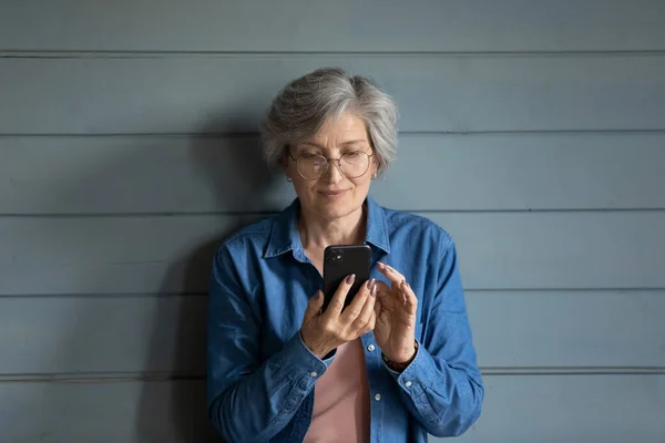 Donna di mezza età che indossa occhiali tenere smartphone focalizzata sullo schermo — Foto Stock