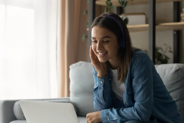 Крупным планом улыбающаяся женщина в наушниках болтает, используя ноутбук — стоковое фото
