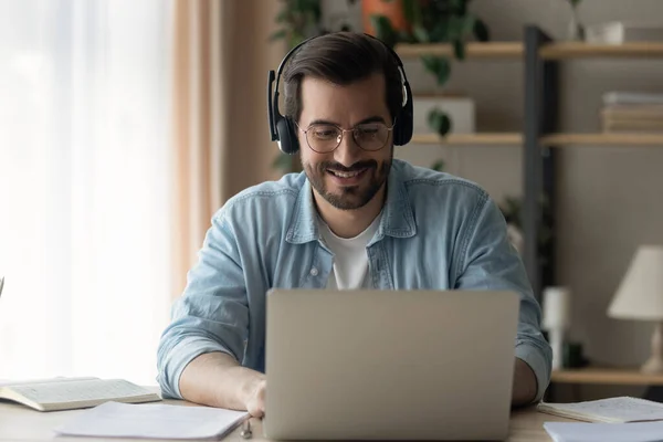 Close up uomo sorridente indossando occhiali e cuffie utilizzando il computer portatile — Foto Stock