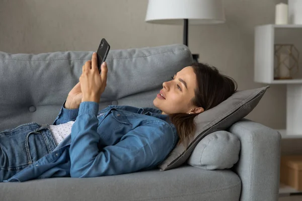 Zblízka usměvavá žena pomocí telefonu, relaxační, ležící na gauči — Stock fotografie