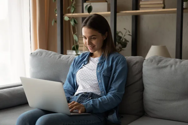Närbild leende kvinna med bärbar dator, sitter på soffan — Stockfoto
