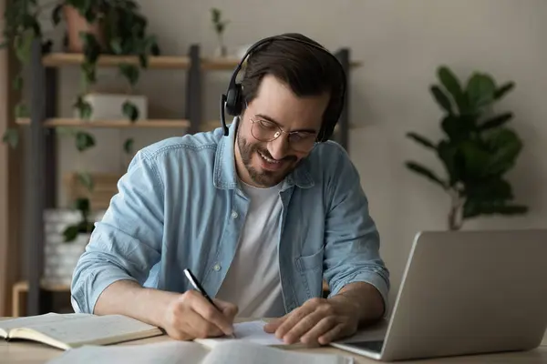 Close up smiling man wearing headphones taking notes, studying online — Stock Photo, Image