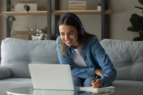 Närbild leende kvinna bär hörlurar med hjälp av laptop, anteckna — Stockfoto