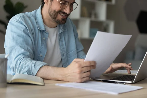 Close up smiling businessman using laptop, holding paper documents — Stock Photo, Image