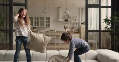 Çocuklar kanepede yastık savaşı yaparken eğleniyorlar.