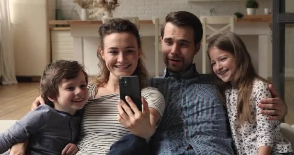 Coppia e figli riposano sul divano divertendosi con lo smartphone — Video Stock