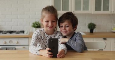 Gülümseyen küçük çocuk ve kız akıllı telefon kullanarak online oyunlar oynuyorlar.