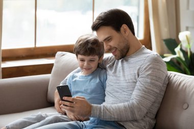 Gülümseyen beyaz bir baba ve küçük bir oğul cep telefonu kullanıyor.