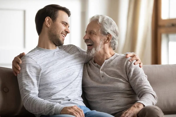 Uśmiechnięty stary tata i dorosły syn relaksują się w domu — Zdjęcie stockowe