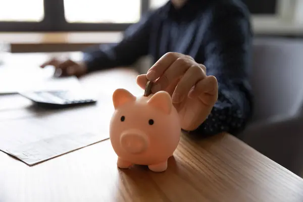 Close up woman putting coin into pink piggy bank