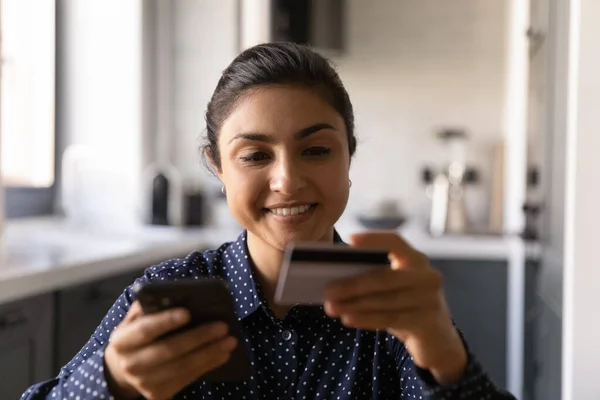 Close up happy Indian woman holding credit card, using phone — Stock Photo, Image