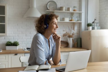 Gülümseyen genç kadın dizüstü bilgisayarda çalışıyor evde hayal kuruyor