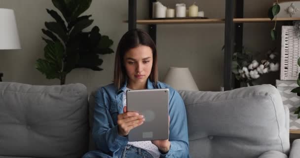 Vrouw zitten op de bank houden tablet apparaat met behulp van online diensten — Stockvideo