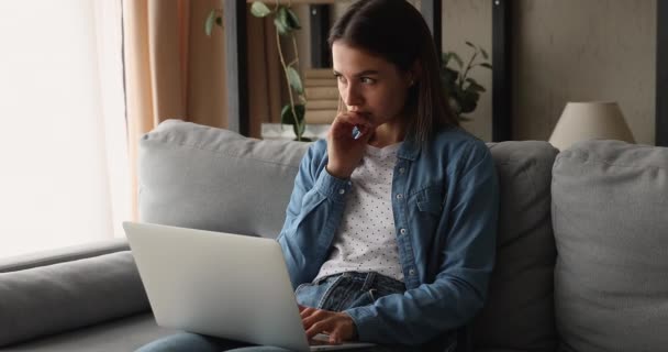 Sérieux jeune femme assis sur le canapé travail sur ordinateur portable — Video