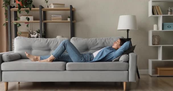Молодая женщина с закрытыми глазами лежит на удобном диване одна — стоковое видео