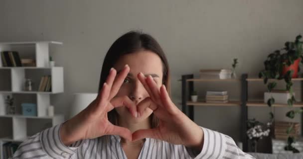Красивая молодая женщина соединяет пальцы, показывая форму сердца перед камерой — стоковое видео